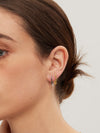 Close-up of a person wearing gold and silver hoop earrings with a neutral background