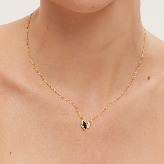 Gold necklace with a small leaf-like pendant on a person wearing a white top.