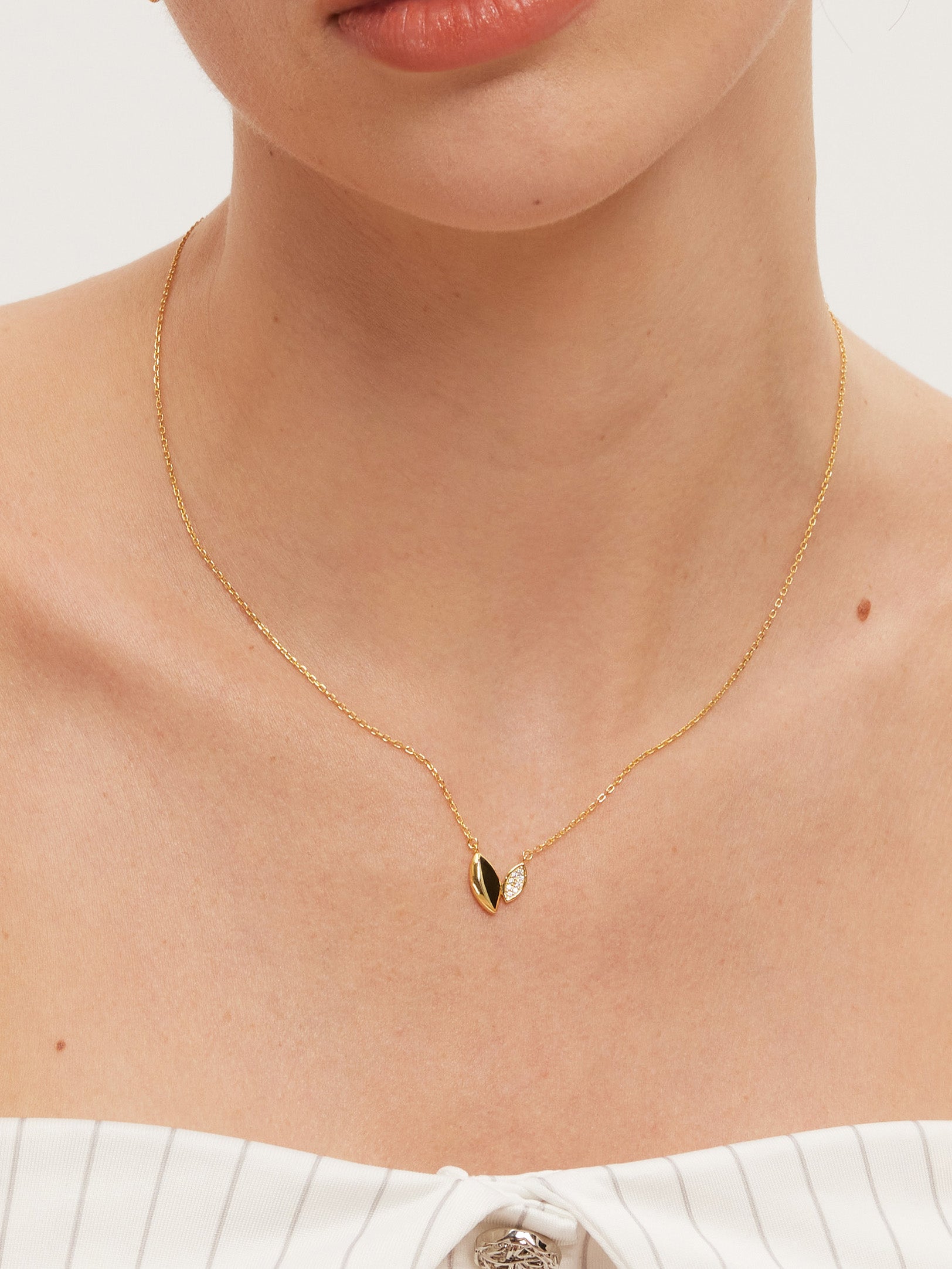 Gold necklace with a small leaf-like pendant on a person wearing a white top.