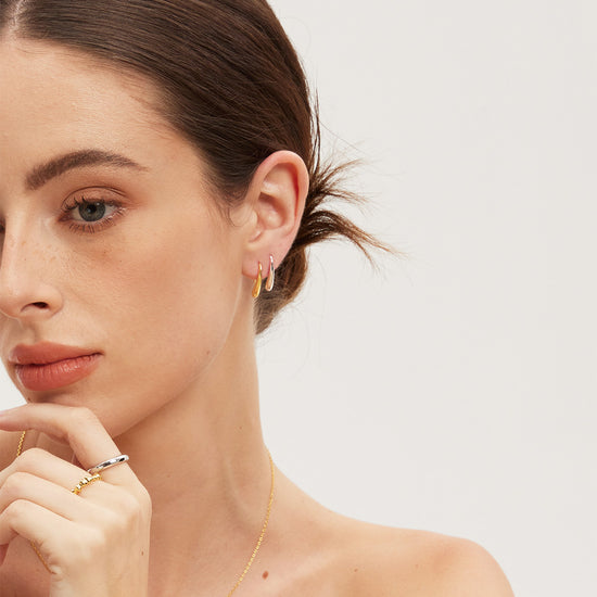 Woman wearing gold and silver jewelry including earrings and a necklace on a plain background