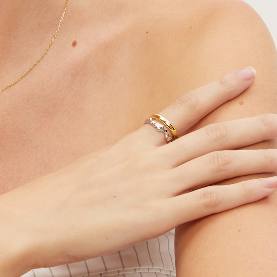 Close-up of a person wearing two gold and silver rings on a plain background