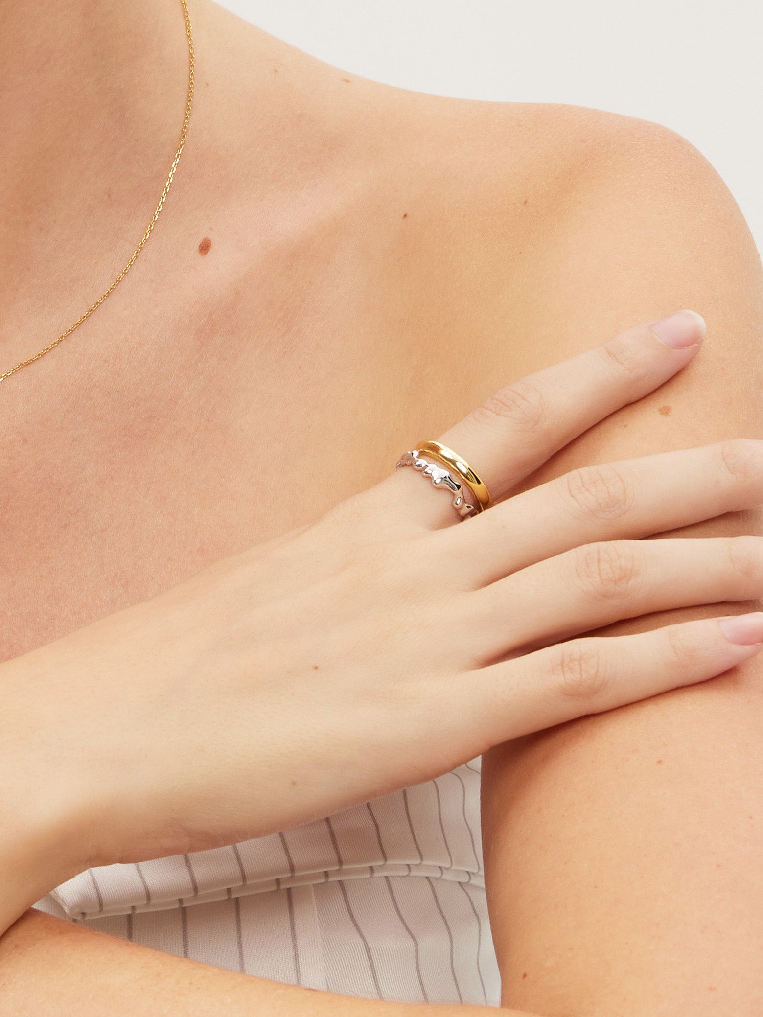 Close-up of a person wearing two gold and silver rings on a plain background