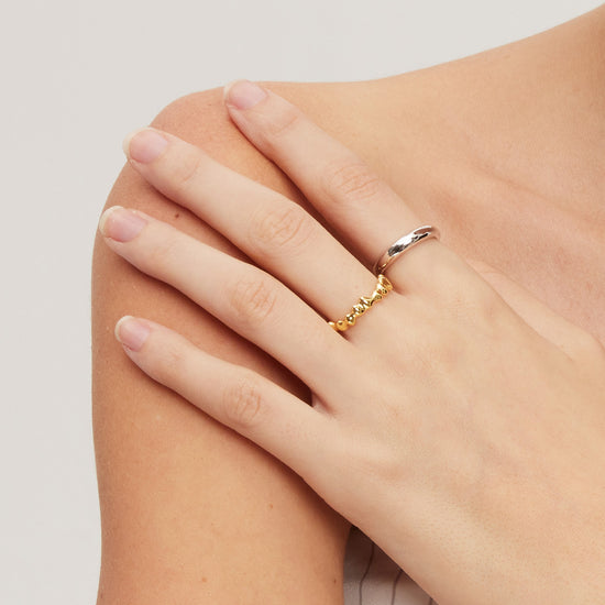 Hand wearing a gold molten ring on a light background