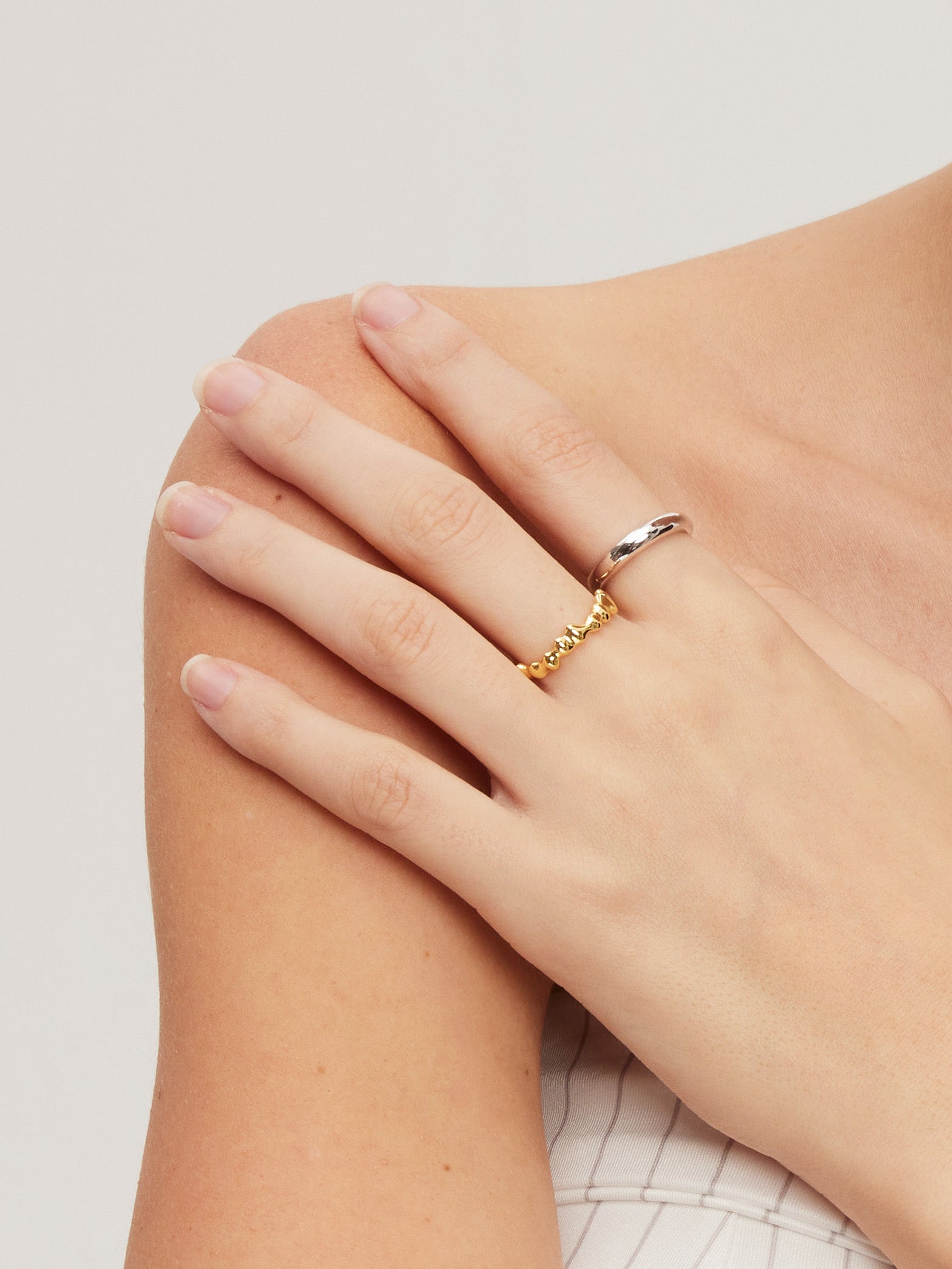 Hand wearing a gold molten ring on a light background