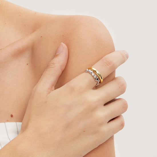 Hand wearing gold and silver rings on a light background