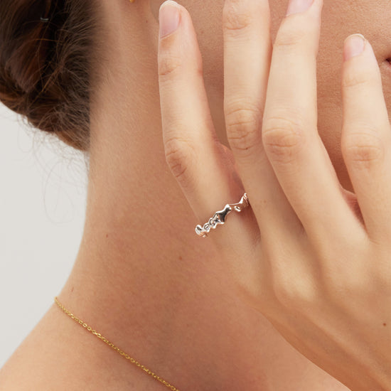 Close-up of a hand wearing a silver molten ring with a gold necklace and earring.