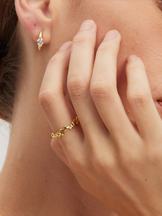 Close-up of a hand wearing a gold molten ring with an earring in the background.