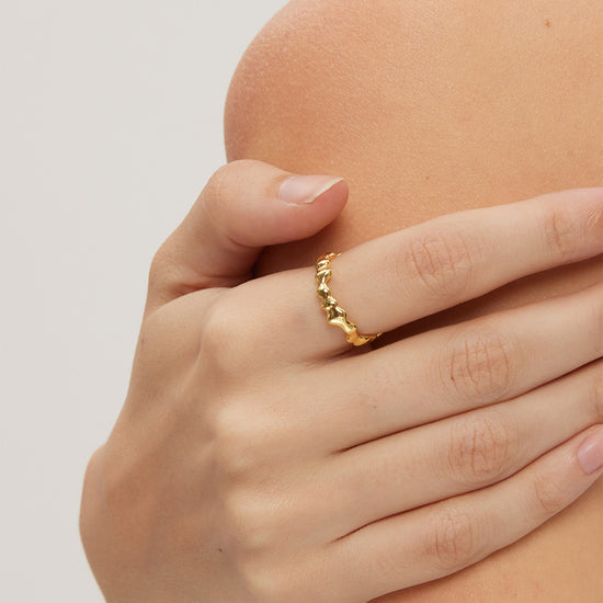 Hand wearing a gold ring on a neutral background