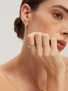Close-up of a woman wearing gold earrings, silver classic ring, and necklace on a neutral background