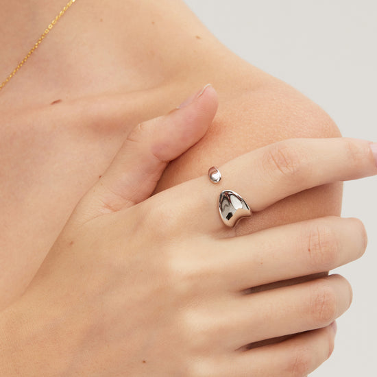 Hand wearing a silver ring with a heart design on a neutral background