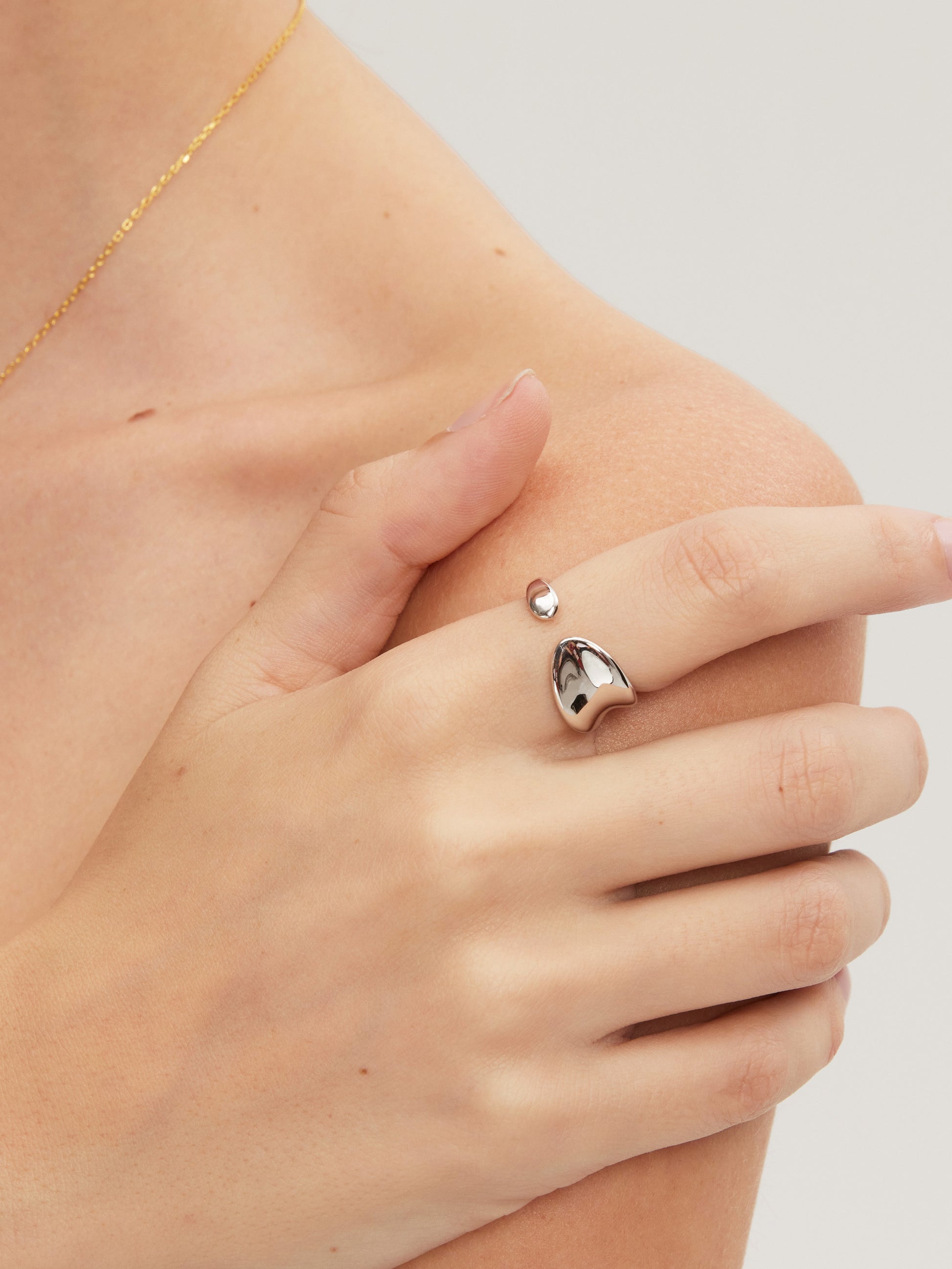Hand wearing a silver ring with a heart design on a neutral background