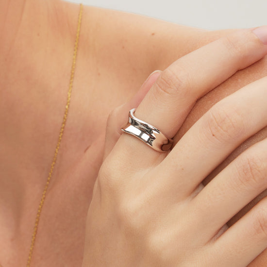 Silver ring on a finger with a gold necklace in the background