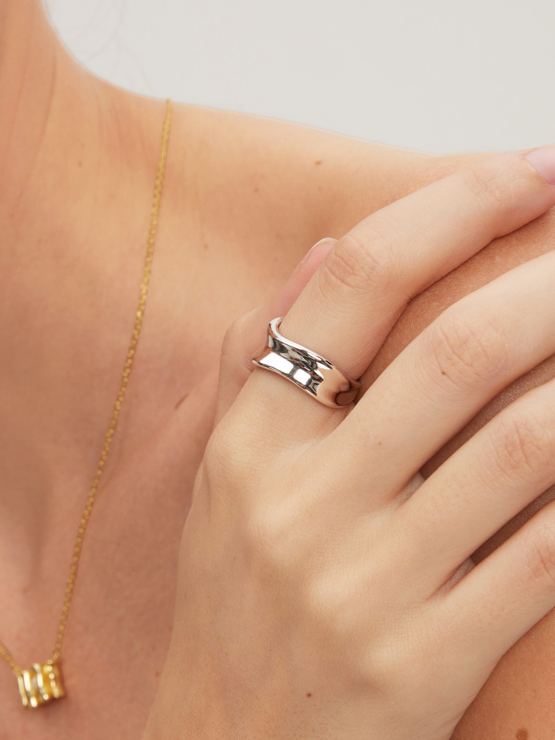 Silver ring on a finger with a gold necklace in the background