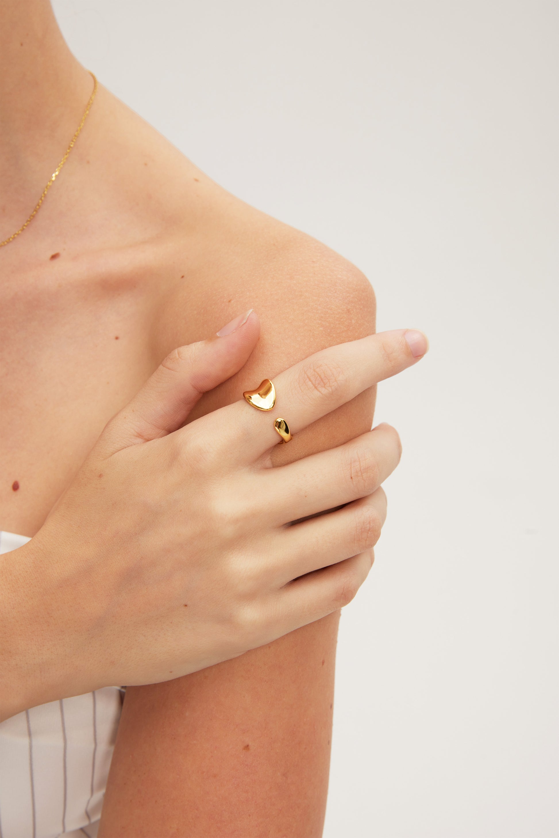 Gold ring with a heart design worn on a finger against a neutral background