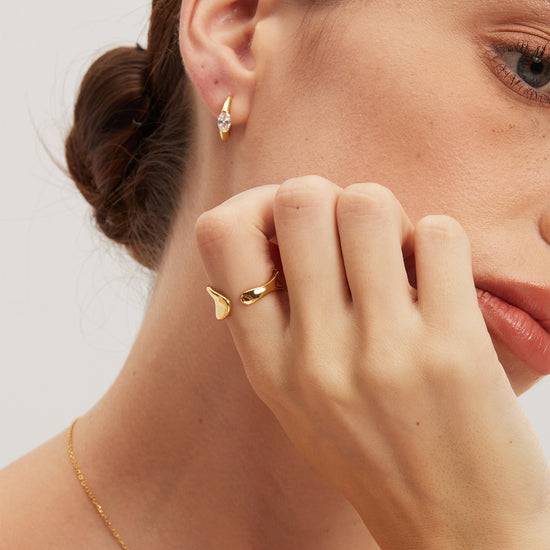 Close-up of a woman wearing gold jewelry including earrings, a ring, and a necklace.