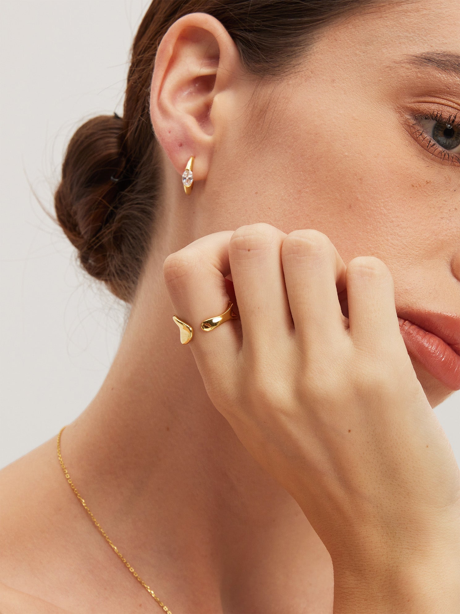 Close-up of a woman wearing gold jewelry including earrings, a ring, and a necklace.