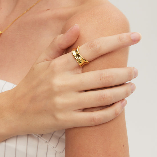 Close-up of a hand wearing a gold ring on a light background