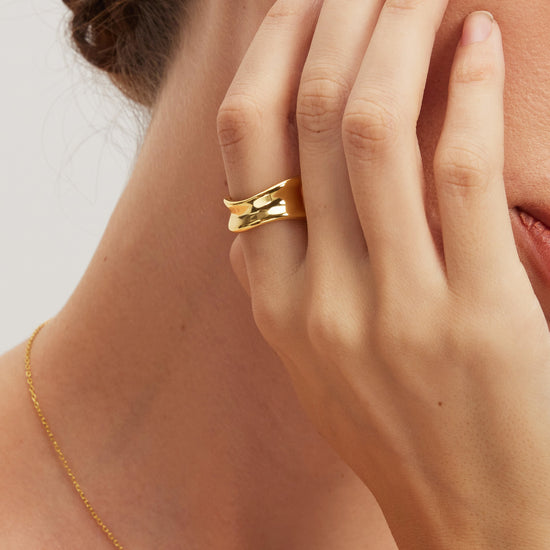 Close-up of a person wearing gold jewelry including an earring, ring, and necklace.