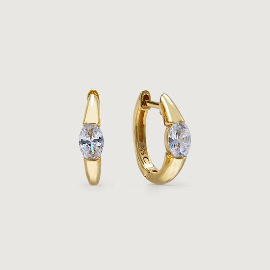 Gold hoop earrings with clear gemstones on a light beige background