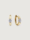 Gold hoop earrings with clear gemstones on a light beige background