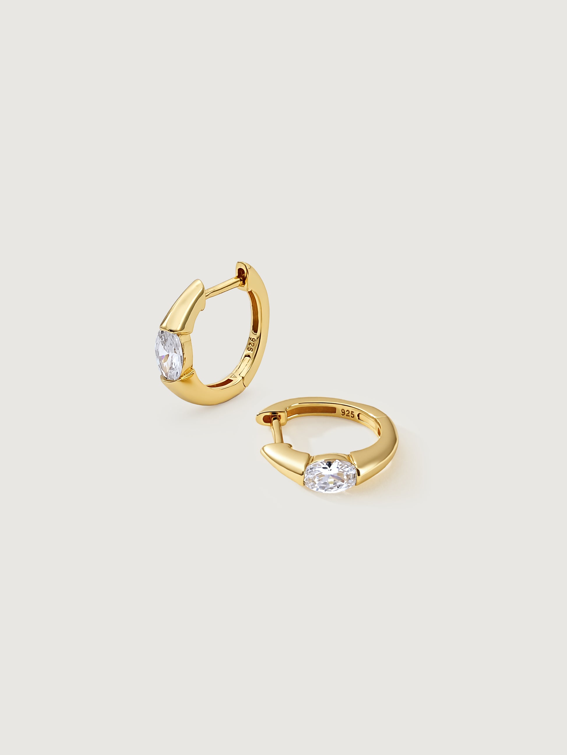 Gold hoop earrings with clear gemstones on a light gray background