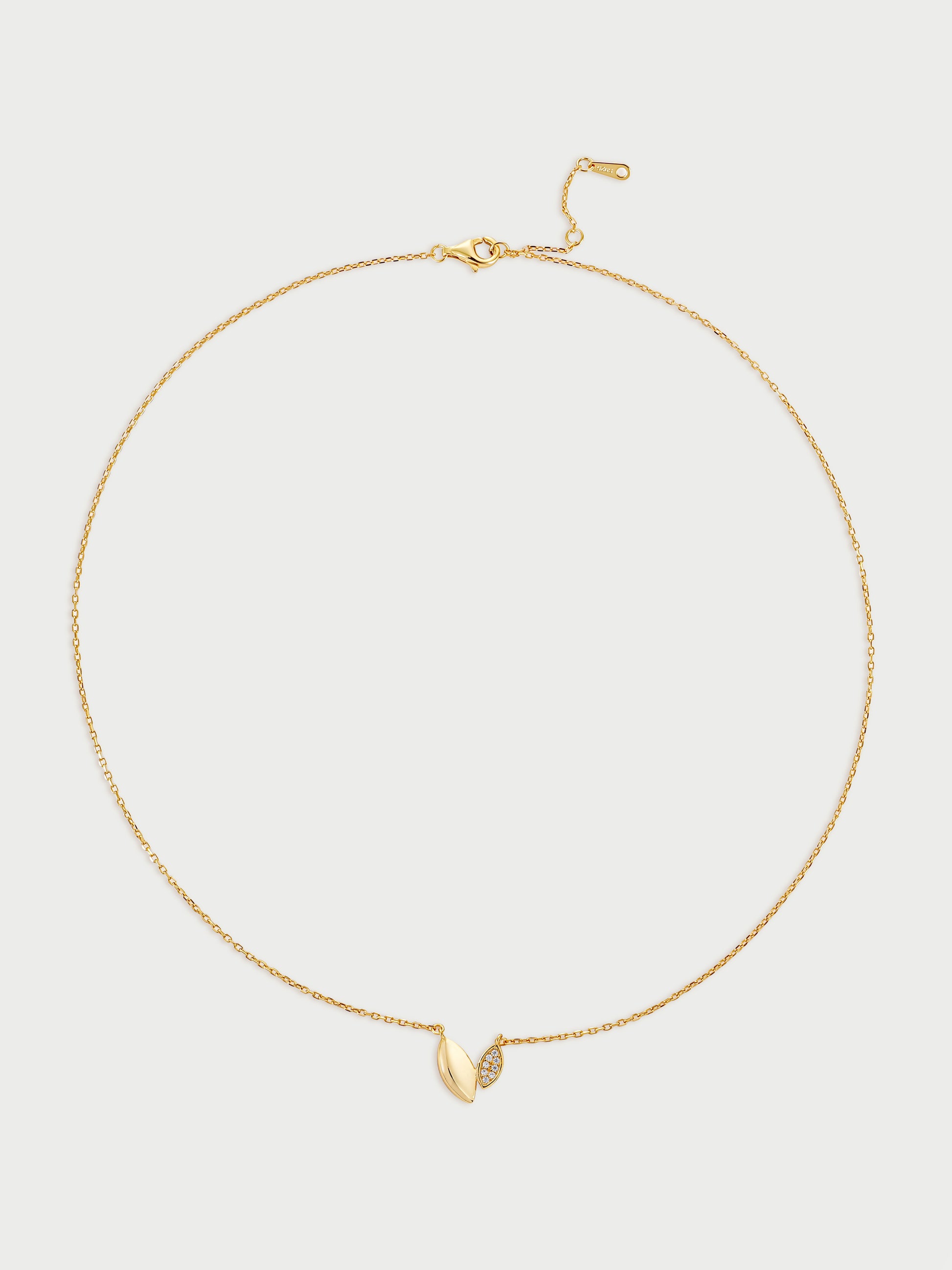 Gold necklace with a small leaf-like (also heart-like) pendant on a light gray background
