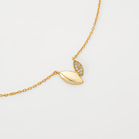 Gold necklace with a leaf-shaped pendant on a light gray background